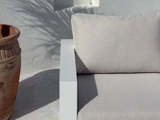 A close-up of a modern outdoor sofa cushion in a light beige textured fabric, set against a white wall. 