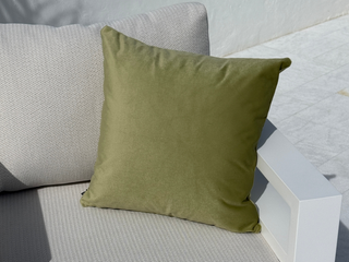 An olive green square throw pillow displayed on a light gray textured outdoor sofa with a white armrest. 