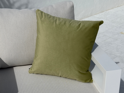 An olive green square throw pillow displayed on a light gray textured outdoor sofa with a white armrest. 